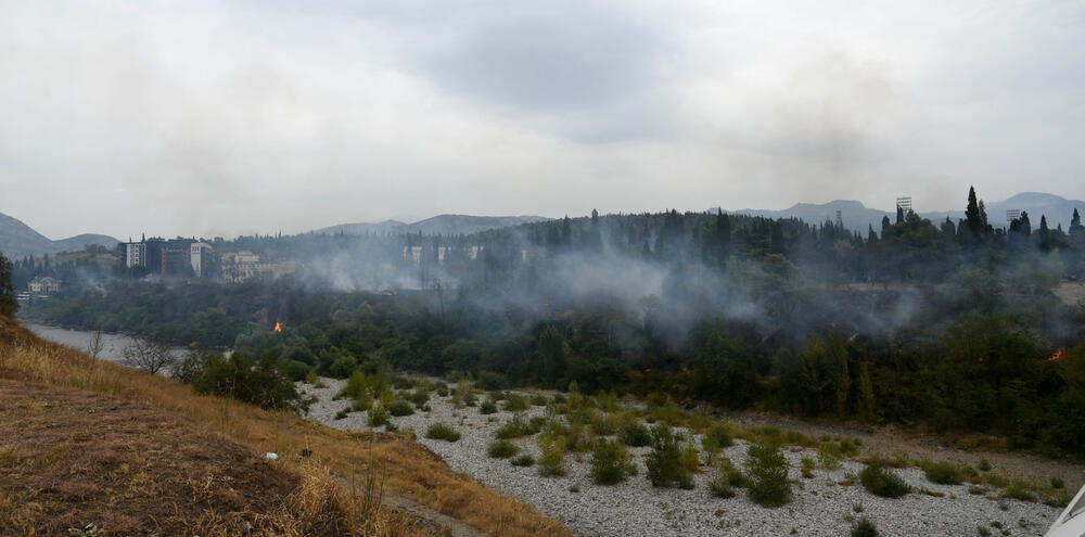 <p>Podgorički vatrogasci gase vatru koja je zahvatila travu, nisko rastinje i drveće i u blizini centra pored mosta Milenijuma</p>