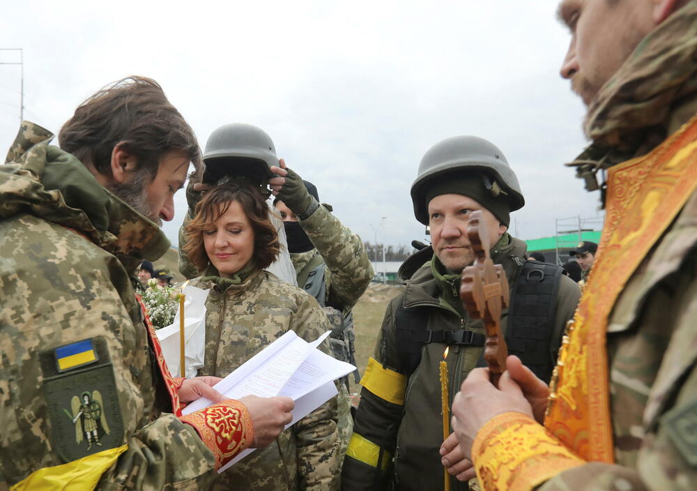 <p>Pripadnici ukrajinskih snaga teritorijalne odbrane Lesija Ivaščenko i Valerij Filimonov razmjenjuju prstenje na svom vjenčanju tokom sukoba između Ukrajine i Rusije, na kontrolnom punktu u Kijevu. U toku ceremonije bili su okruženi drugim pripadnicima ukrajinskih oružanih snaga, a prisutan je bio i gradonačelnik Kijeva Vitalij Kličko.</p>