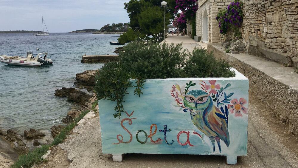 <p>Nenašminkane kuće od kamena, stare masline i smokve, makija. More miluje stijene. Zimzeleno rastinje, izraslo na vjetru, nadnijelo se nad kristalnobistru vodu. Jedan se čovjek zabavio čišćenjem svoje barke u luci</p>