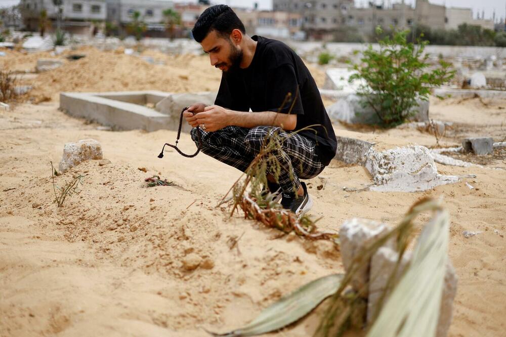 The uncle of a Palestinian girl, who died days after being rescued from her dying mother's womb, crouches next to her grave in Rafah in the southern Gaza Strip, Photo: Reuters