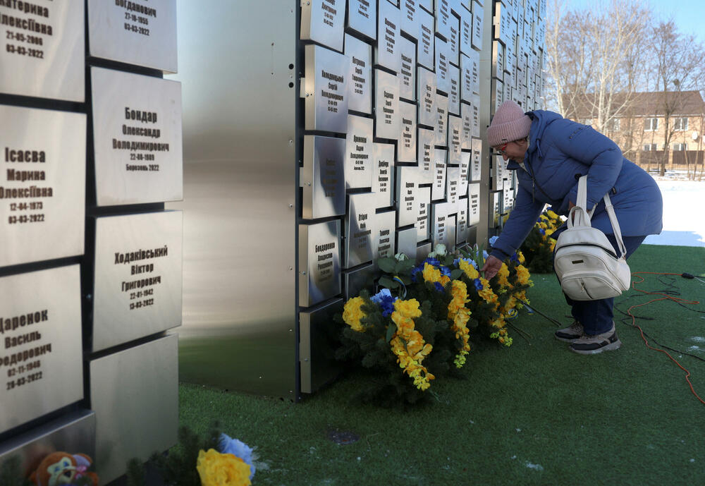 Žena polaže cvijeće na spomen-obilježje masovne grobnice povodom treće godišnjice ruske invazije na Ukrajinu u Buči