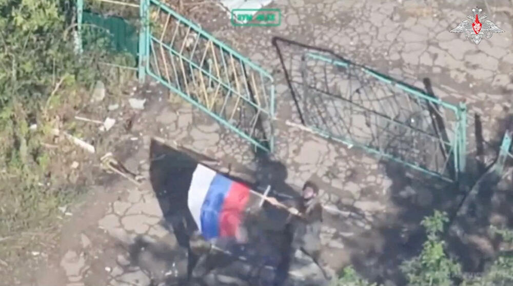 Ruski vojnik maše ruskom zastavom u blizini oštećenih zgrada u Kostjantinivki