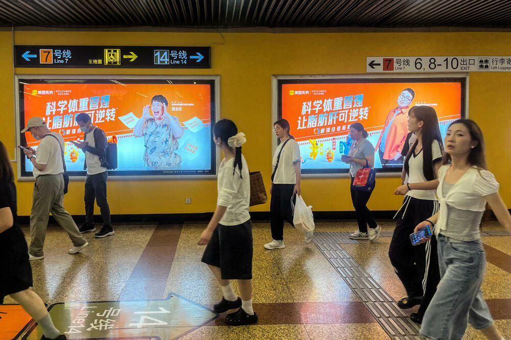 Ljudi prolaze pored bilborda kompanija Inovent Bajolodžiks i Meituan, postavljenih na zidu stanice metroa u Šangaju, u Kini, Foto: Reuters